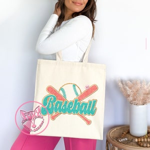 May include: A beige canvas tote bag with a graphic design of two crossed baseball bats and a baseball with the word "Baseball" in teal and gold lettering.