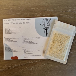 May include: A white resealable bag containing a sourdough starter, a white paper with instructions for feeding and maintaining the starter, and a whisk illustration. The instructions include the text "You now have your sourdough starter. What do you do now? ..." and details for each day of the starter's development.