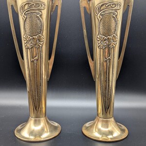 May include: A pair of antique brass vases with ornate floral designs and two handles. The vases are tall and slender with a flared base.