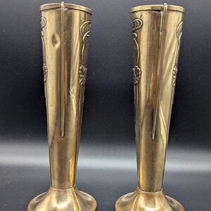K&ouml;nnte beinhalten: Ein Paar goldene Metall-Blumenvasen mit einem verzierten Design. Die Vasen sind hoch und schlank mit einem ausgestellten Fu&szlig;.
