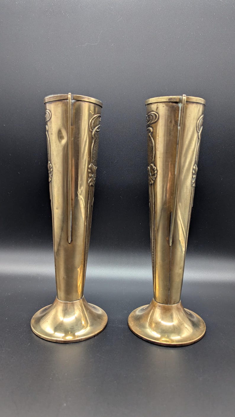 K&ouml;nnte beinhalten: Ein Paar goldene Metall-Blumenvasen mit einem verzierten Design. Die Vasen sind hoch und schlank mit einem ausgestellten Fu&szlig;.