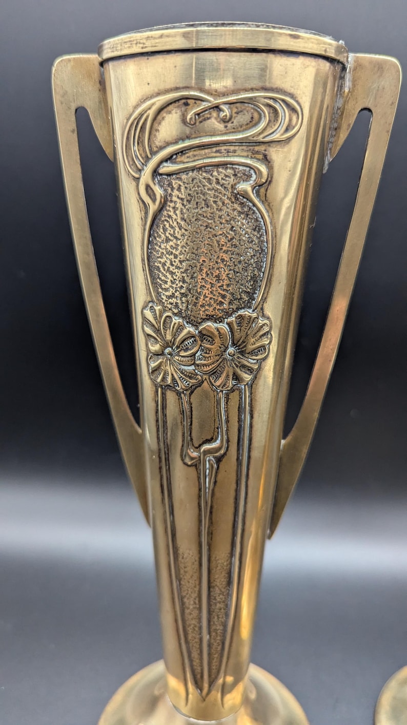 K&ouml;nnte beinhalten: Zwei antike Messingvasen mit kunstvollen Jugendstil-Designs. Die Vasen haben eine geh&auml;mmerte Textur und zeigen florale Motive.