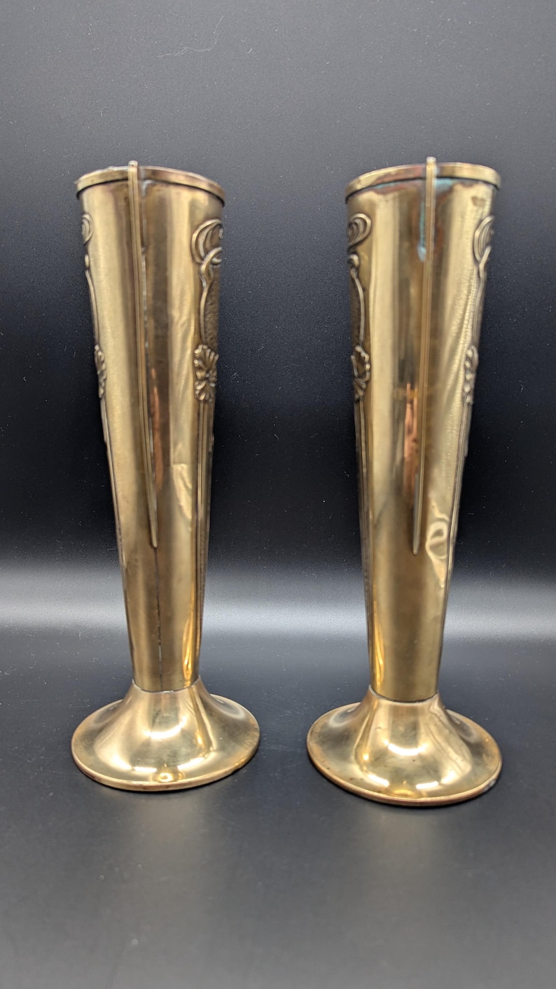 K&ouml;nnte beinhalten: Ein Paar goldfarbene Metallvasen mit einem verzierten Design. Die Vasen sind hoch und schlank mit einem ausgestellten Fu&szlig;.