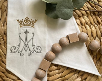 May include: White fabric with a gold crown and embroidered "M" with a wooden bead garland.