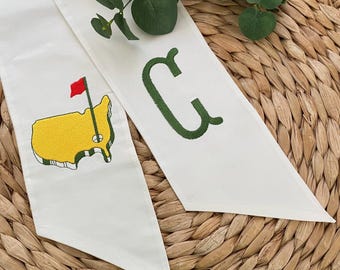 May include: White fabric sash with green embroidered letter "C" and a yellow embroidered outline of the United States with a red flag and golf hole.