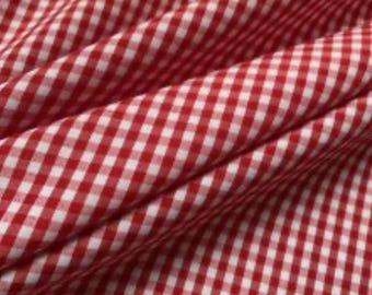 May include: Close-up of red and white gingham fabric. The fabric is folded, creating diagonal lines across the image. The pattern is a classic checkered design, with evenly spaced squares of red and white.
