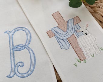 May include: White fabric with blue embroidered letter B and a cross with a blue and white scarf and a white lamb standing next to it.