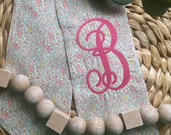 May include: Two fabric ribbon ties with a floral pattern and a pink embroidered letter "B" on one tie.