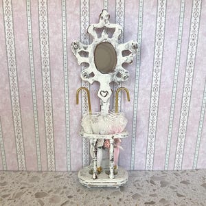 May include: White painted wooden umbrella stand with a mirror and a heart design. The stand has two gold hooks for hanging umbrellas and a shelf for storing umbrellas.