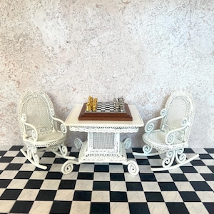 May include: White wicker rocking chairs and a white wicker table with a chessboard and gold chess pieces on top. The chairs and table are on a black and white checkered floor.
