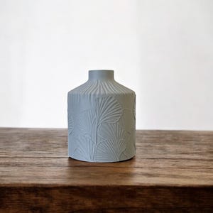 May include: A light gray ceramic vase with a textured surface and a design of ginkgo leaves.