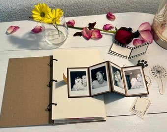 May include: A brown leather-bound journal with a white interior and a set of black metal rings. The journal is open to reveal a mini photo album with black and white photos of a woman and a dog.