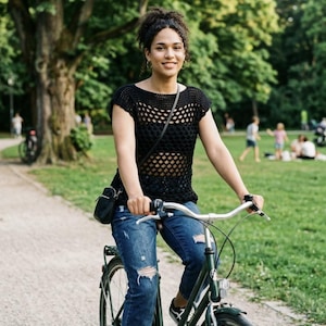 Könnte beinhalten: Eine Person fährt mit einem grünen Fahrrad auf einem Schotterweg in einem Park. Sie trägt ein schwarzes Mesh-Top, blaue zerrissene Jeans und schwarz-weiße Turnschuhe. Im Hintergrund sind Bäume und andere Personen zu sehen.