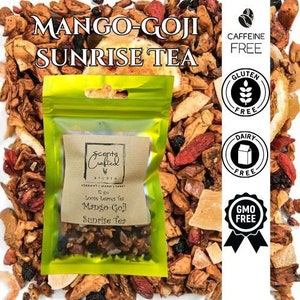 May include: A close-up of loose leaf tea with the text "MANGO-GOJI SUNRISE TEA". The tea is in a clear bag with a brown paper label that reads "Scents Crafted". The image also includes icons for caffeine, gluten, dairy, and GMO free.