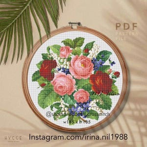 May include: A circular wooden embroidery hoop containing a cross-stitch pattern of a floral bouquet with pink and red roses, white lily of the valley, and blue flowers. The text reads PDF PATTERN FILE, @shomaredoozi_crossstitch, w185 x h185.