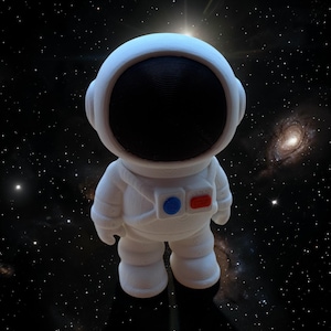 May include: A white astronaut figurine with a black visor and a space-themed background. The astronaut suit has blue and red accents. The figurine is a decorative item.