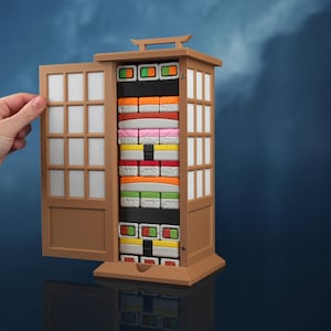 May include: A brown, rectangular storage cabinet with a hinged door featuring a grid pattern. The interior contains multiple stacked rows of colorful, rectangular blocks resembling various types of sushi, including orange, pink, white, and green pieces.