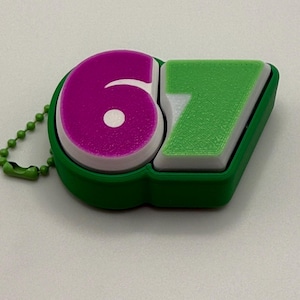 Puede incluir: Un llavero verde y blanco con los números "67". El número "6" es magenta, y el "7" es verde. El llavero tiene un borde verde y una cadena de bolas verde.