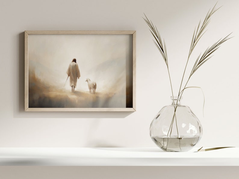 May include: A framed painting of a person in a white robe walking with a white lamb in a misty landscape. The painting is hanging on a white wall above a white shelf with a clear glass vase filled with dried grass.