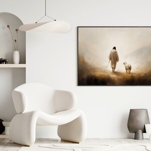 May include: A framed painting depicting a person in a white robe walking with a white sheep in a misty landscape. The painting is hanging on a white wall in a modern living room setting.