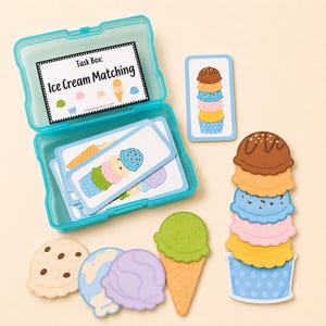 以下が含まれることがあります： Task Box: Ice Cream Matchingと書かれたラベル付きのターコイズブルーのプラスチック製収納ボックス。中にはアイスクリームのイラストが描かれた長方形のカードが入っています。ボックスの横には、紙製の切り抜きアイスクリームのスクープ、ワッフルコーン、積み重なったスクープが置かれています。