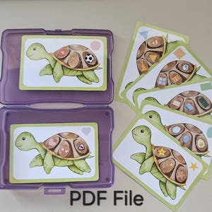 May include: Illustrated cards with cartoon turtles, each with a unique shell design. The cards are in a purple plastic case and spread out. The text "PDF File" is visible. The cards are on a light surface.
