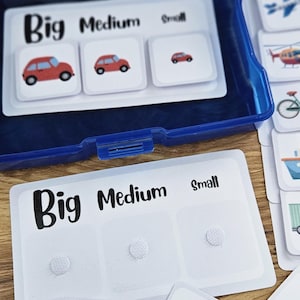 May include: A blue plastic box containing cards for a sorting game. The cards are labeled "Big," "Medium," and "Small" with vehicle illustrations. A yellow school bus is shown on a card.