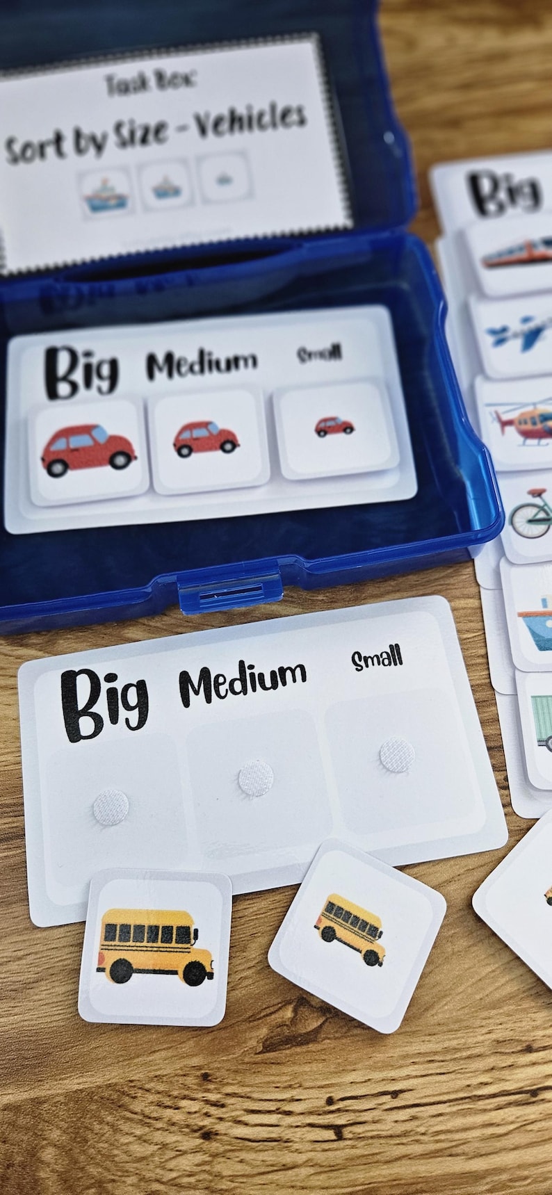 May include: A blue plastic box containing cards for a sorting game. The cards are labeled "Big," "Medium," and "Small" with vehicle illustrations. A yellow school bus is shown on a card.