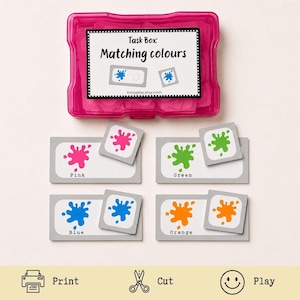 May include: A pink plastic task box labeled Task Box: Matching colours with a set of rectangular cards featuring paint splatters in pink, green, blue, and orange. Each card includes the corresponding color name printed in black text below the graphic.