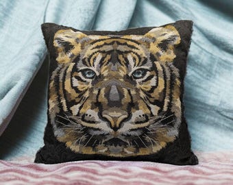 May include: Square decorative pillow featuring a detailed tiger face design. The pillow has a black background with a woven image of a tiger's face in shades of brown, tan, and gray, with blue eyes. The pillow is placed on a patterned surface.