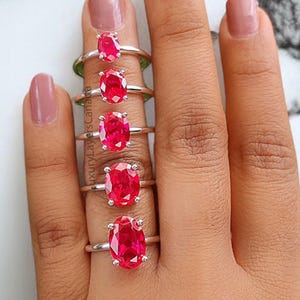 May include: A set of seven silver rings with oval-shaped red gemstones. The rings are arranged in order of size, with the smallest ring on the left and the largest ring on the right.