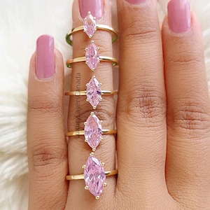 May include: A set of five gold rings with pink marquise-shaped stones. The rings are arranged in order of size, with the smallest ring on the left and the largest ring on the right.