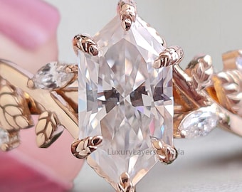 May include: A rose gold engagement ring featuring a large, clear, rectangular-cut center stone. The band is adorned with delicate leaf and vine details, and smaller accent stones. The ring has a nature-inspired design.
