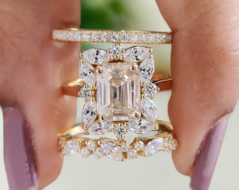 May include: A gold ring set with a large, square-shaped diamond surrounded by smaller diamonds. The ring is part of a three-ring set, with two smaller bands featuring smaller diamonds.