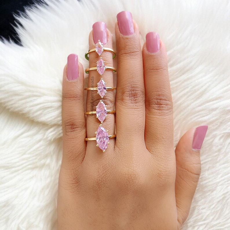 May include: A set of five gold rings with pink marquise-shaped stones. The rings are arranged in order of size, with the smallest ring on the left and the largest ring on the right.