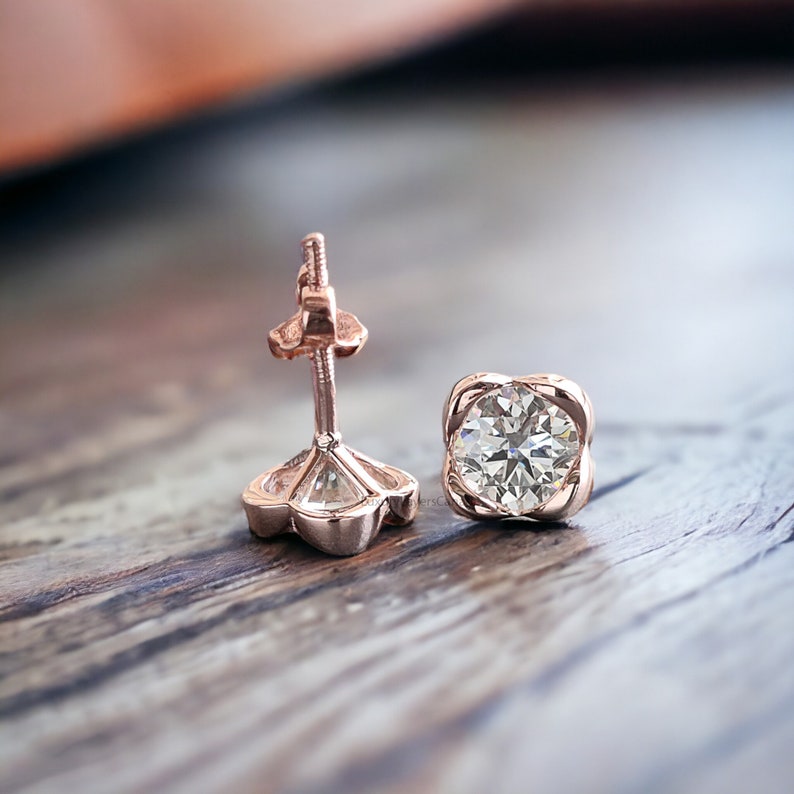 May include: A pair of rose gold stud earrings with a round, clear diamond in each setting. The earrings have a simple, elegant design.