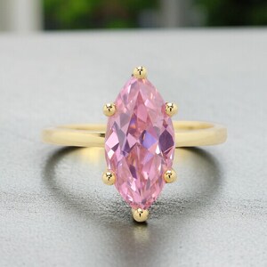 May include: A gold ring with a large pink marquise-shaped gemstone. The ring has a simple band and the gemstone is set in a prong setting.