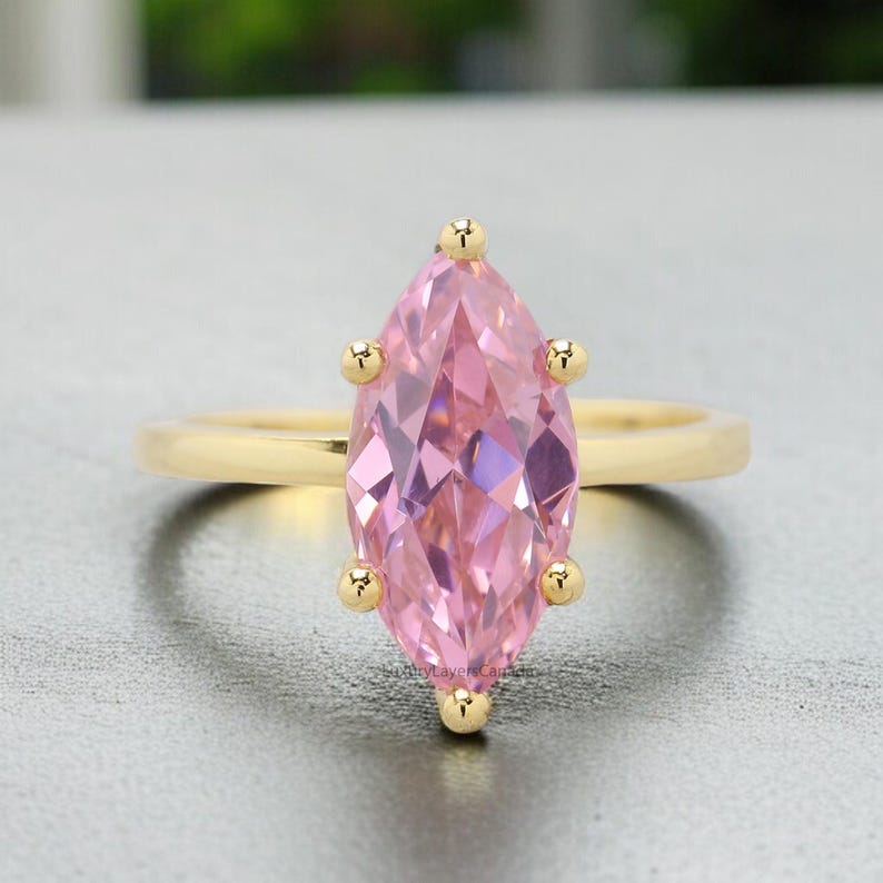 May include: A gold ring with a large pink marquise-shaped gemstone. The ring has a simple band and the gemstone is set in a prong setting.