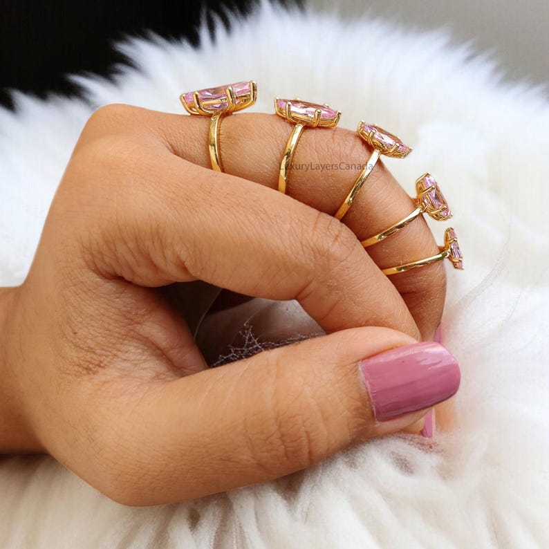 May include: A set of five gold rings with pink gemstone accents. The rings are stacked on a finger, with the largest ring at the base and the smallest ring at the top.