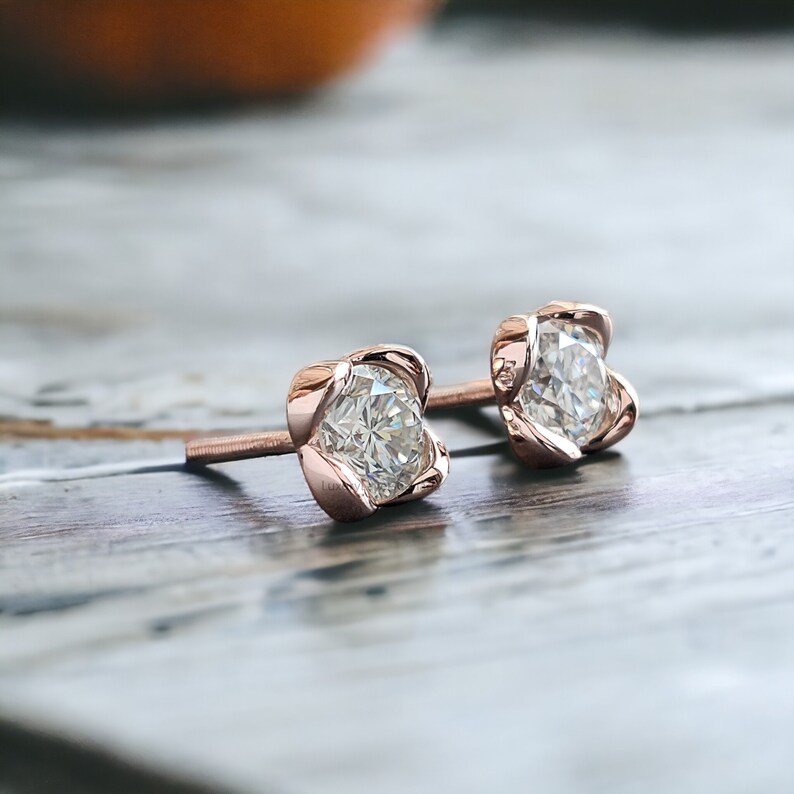 May include: A pair of rose gold stud earrings with a clear round gemstone set in a four-prong setting. The earrings have a delicate floral design.