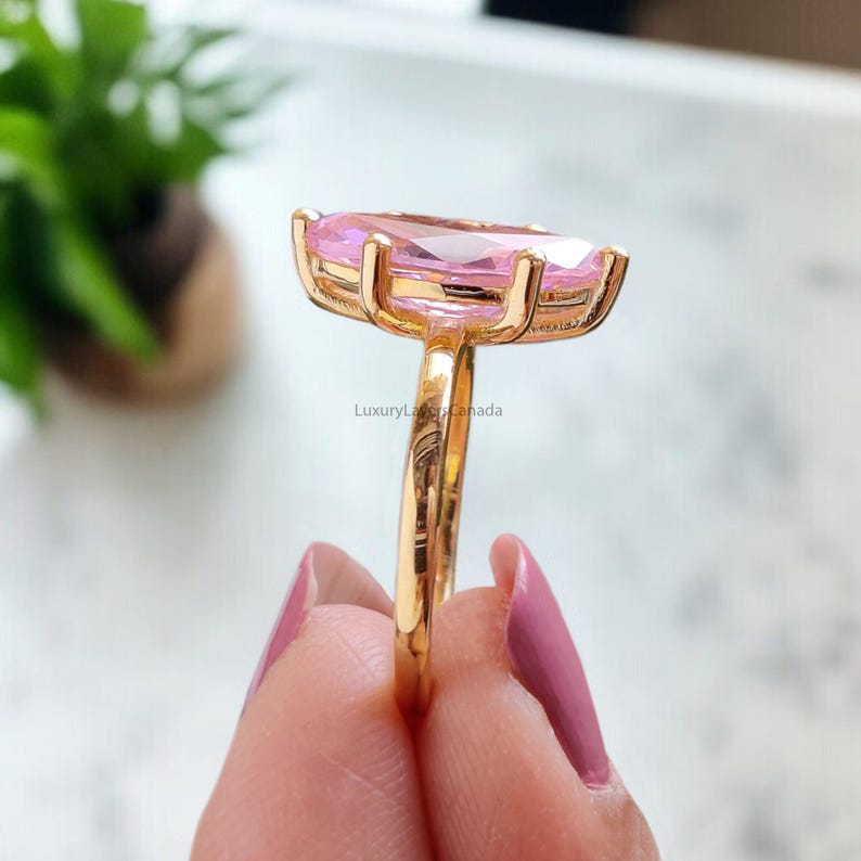 May include: A gold ring with a large, oval-shaped pink gemstone. The ring is set with smaller gemstones around the main stone.