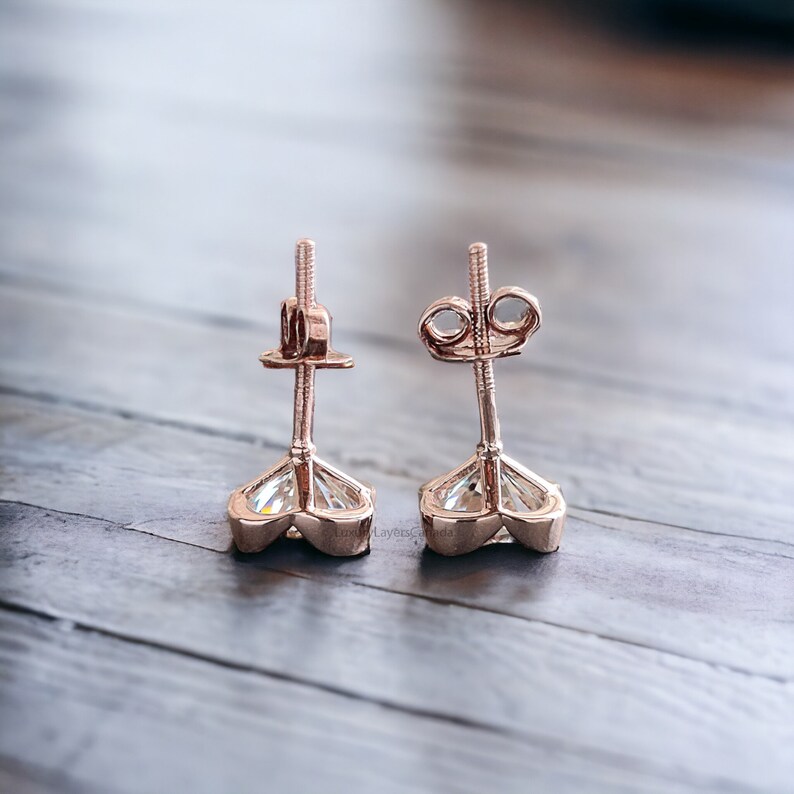 May include: A pair of rose gold stud earrings with a clear heart-shaped gemstone. The earrings have a post and butterfly back.
