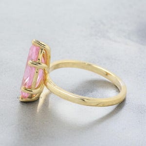 May include: A gold ring with a large, pink, faceted gemstone. The ring is set in a simple, classic style.
