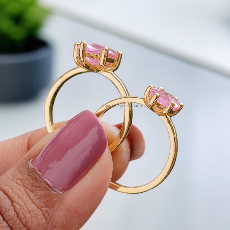 May include: Two gold rings with pink gemstone settings. The rings are stacked on top of each other.
