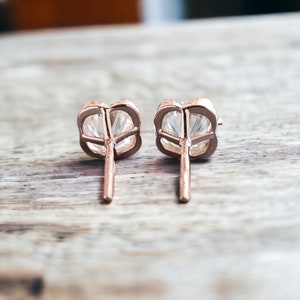 May include: A pair of rose gold stud earrings with a clear round gemstone in each earring.