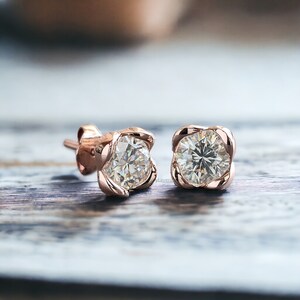 May include: A pair of rose gold stud earrings with a clear round gemstone set in a delicate flower-shaped design.