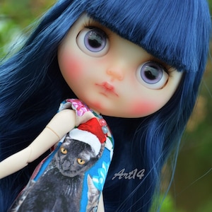 May include: A Blythe doll with blue hair and large purple eyes. The doll wears a dress featuring a black cat wearing a Santa hat. The dress has a blue floral background and the text "Art14".