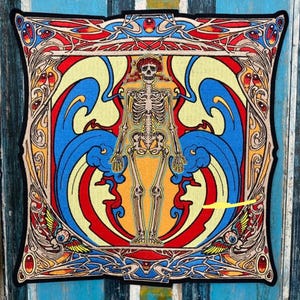 May include: A decorative square pillow featuring a colorful, stylized skeleton design. The artwork includes a skeleton figure in the center, surrounded by blue wave-like shapes, red and yellow accents, and an ornate border. The pillow has a black border.