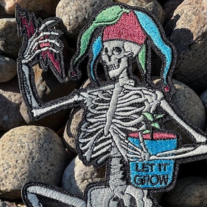 May include: Embroidered patch featuring a skeleton in a jester's hat holding a lightning bolt and a potted plant. The skeleton is white with black outlines. The jester's hat is red, green, and blue. The text "LET IT GROW" is on the pot.