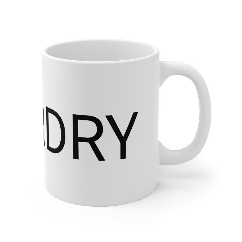 May include: A white ceramic coffee mug with a black, sans-serif DRY text printed on it. The mug has a C-shaped handle. The mug is shown against a white background.